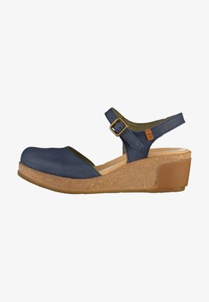 Navy blue leather wedge sandal with ankle strap, bronze buckle, and cork-textured sole, shown from the side.