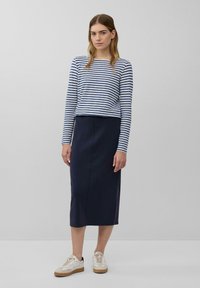 Gestreepte lange mouw top met marineblauwe en witte strepen, gecombineerd met een marineblauwe midi-skirt. Witte sneakers met beige accenten. Eenvoudige en aansluitende silhouet.