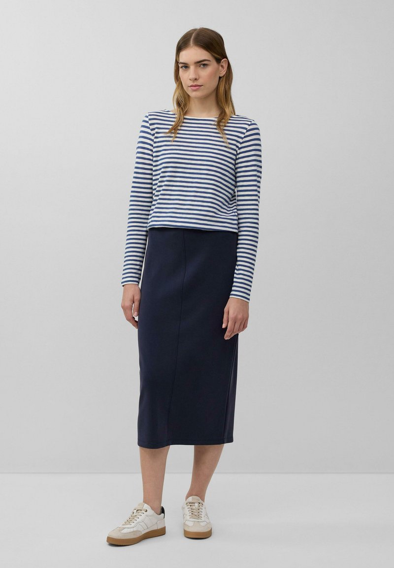 Gestreepte lange mouw top met marineblauwe en witte strepen, gecombineerd met een marineblauwe midi-skirt. Witte sneakers met beige accenten. Eenvoudige en aansluitende silhouet.