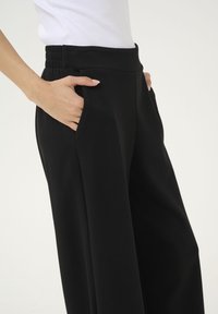 Pantaloni larghi neri realizzati in morbido tessuto, con vita alta e dettagli arricciati e tasche laterali.