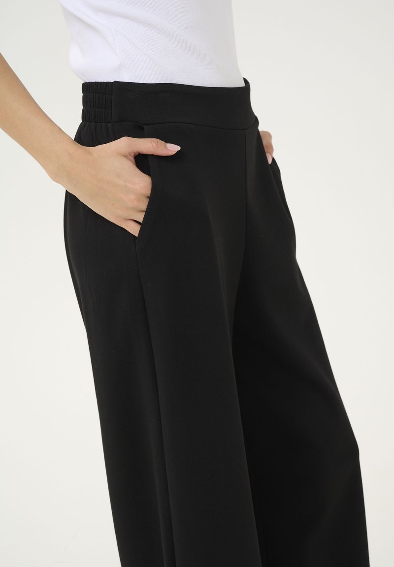 Schwarze weit geschnittene Hose aus weichem Stoff, featuring einen hohen Bund mit gerafften Details und seitlichen Taschen.