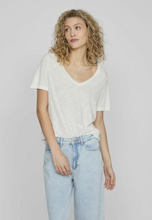 Camiseta blanca de cuello en V de manga corta, ligera y con un ajuste relajado, combinada con jeans de mezclilla de tiro alto en azul claro. Textura suave, sin estampados.