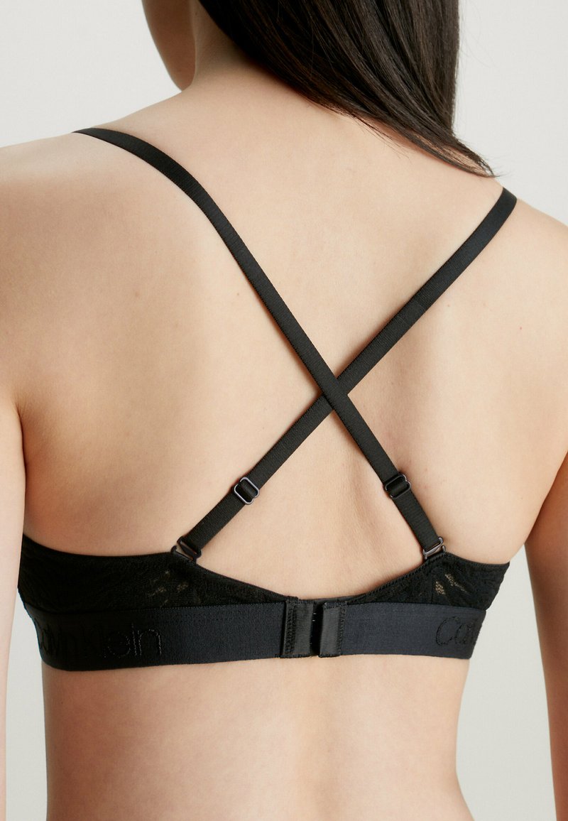 Schwarzer Spitzen-Bralette mit verstellbaren überkreuzten Trägern. Mit einem glatten Band mit "Calvin Klein"-Logo und einem Hakenverschluss auf der Rückseite.