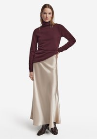 Bourgogne-rullekrave sweater med afslappet pasform kombineret med en silkeagtig beige maxinederdel og brune støvler med hæl. Glatte teksturer og enkle linjer.