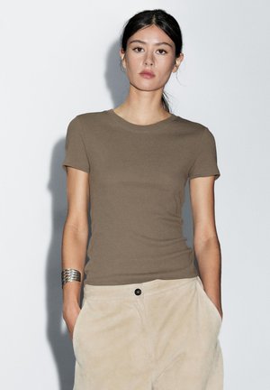 Brown fitted T-shirt with short sleeves, crew neck, and smooth texture, paired with beige pants featuring a front pocket and button.