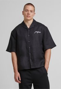 Black short-sleeve button-up shirt in lightweight fabric, featuring a collar and white embroidered text on the left side.