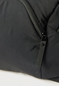 Μαύρη τσάντα με επένδυση, με ανάγλυφη εξωτερική επιφάνεια, αντίθετο φερμουάρ με ματ λεπτομέρεια στο τράβηγμα και δομημένο, γωνιακό σχέδιο.