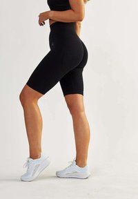 Black high-waisted bike shorts with textured fabric, fitted design, and mid-thigh length, paired with white athletic shoes.