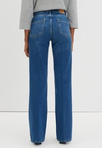 Jean droit taille haute en denim bleu avec une étiquette en cuir à l'arrière de la taille et deux poches arrière. Ourlet propre.