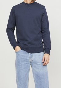 Felpa blu navy in misto cotone, con collo a giro, maniche lunghe e polsini e orlo a coste. Jeans in denim azzurro.