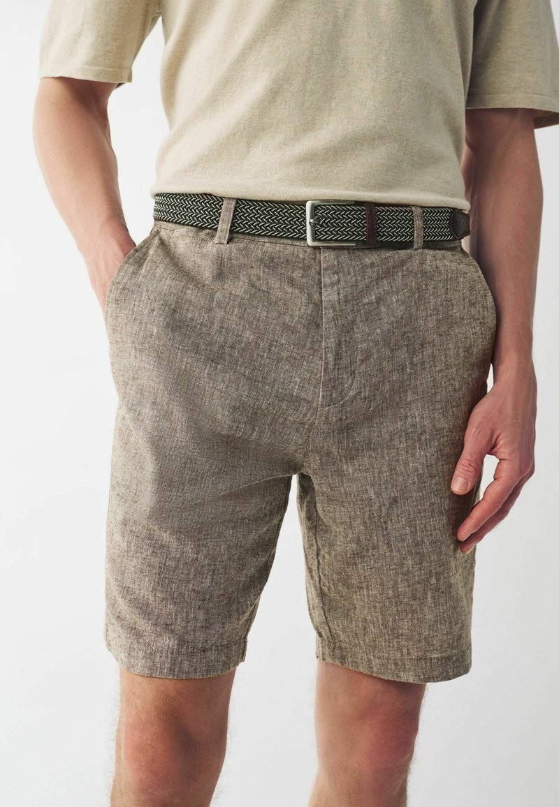 Pantalones cortos de mezcla de lino, marrones con un patrón texturizado, con bolsillos laterales, combinados con un cinturón tejido negro y verde, usados con una camisa gris claro.