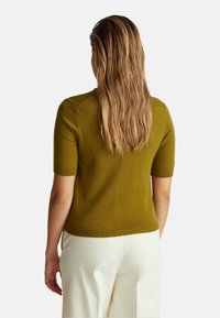 Světle olivový krátký svetr s žebrovanými manžetami a lemem; nošený s krémovými kalhotami; měkká textura, přiléhající střih.