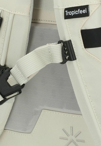 Correa ajustable de tejido beige claro, con una hebilla de plástico negra y un respaldo texturizado. Incluye un parche con el logo de Tropicfeel.