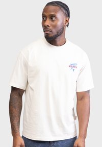 Bombažna kremna majica s kratkimi rokavi, z modrim in rdečim napisom »REBEL« na prsih, z okroglo izrezom in sproščenim krojem.