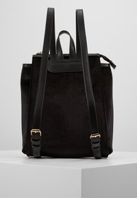 Czarny zamkowy plecak z skórzanymi akcentami, podwójnymi regulowanymi paskami i złotymi detalami. Strukturalny kształt z gładką teksturą.