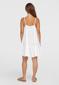 Weißes ärmelloses Kleid mit einem gestuften Rüschensaum, aus leichtem Stoff gefertigt. Verfügt über verstellbare Träger und ein Logoetikett auf der Rückseite.