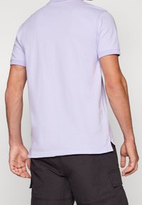 Polo manches courtes lilas avec un col classique, doté d'une texture lisse et de fentes latérales à l'ourlet pour plus de confort.