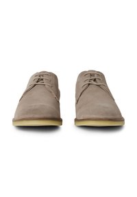 Chaussures en daim beige avec des orteils arrondis, un design à lacets et une semelle en caoutchouc légère. La texture semble douce et lisse.