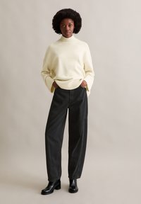 Κρεμ πλεκτό πουλόβερ με ψηλό, ριγωτό γιακά, σε συνδυασμό με μαύρο παντελόνι ψηλής μέσης και φαρδιάς γραμμής, καθώς και γυαλιστερές μαύρες μποτάκια μέχρι τον αστράγαλο.