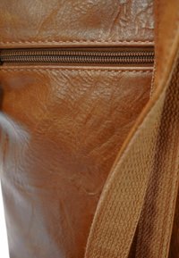 Bruine leren tas met een textuur, uitgerust met een rits aan de bovenkant en een geweven stofband aan één zijde.