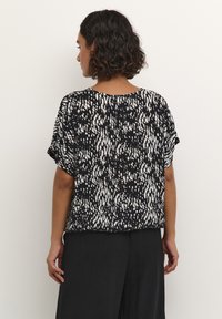Short-sleeve black and white patterned top with a loose fit, featuring a round neckline and smooth fabric, displayed from the back.