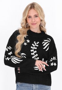Czarny sweter dziewiarski z białą haftowaną florystyką, szerokimi mankietami, ściągaczem u dołu i okrągłym dekoltem. Materiał ma miękką teksturę.