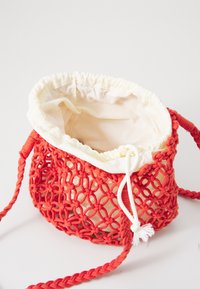 Röd virkad väska med snörning och beige foder. Har en strukturerad, öppen vävdesign och flätade remmar.