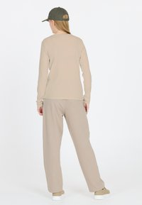 Beige Langarmshirt mit gerippter Struktur und passenden, lockeren beigen Hosen, kombiniert mit einer olivgrünen Kappe und hellen Sneakers.