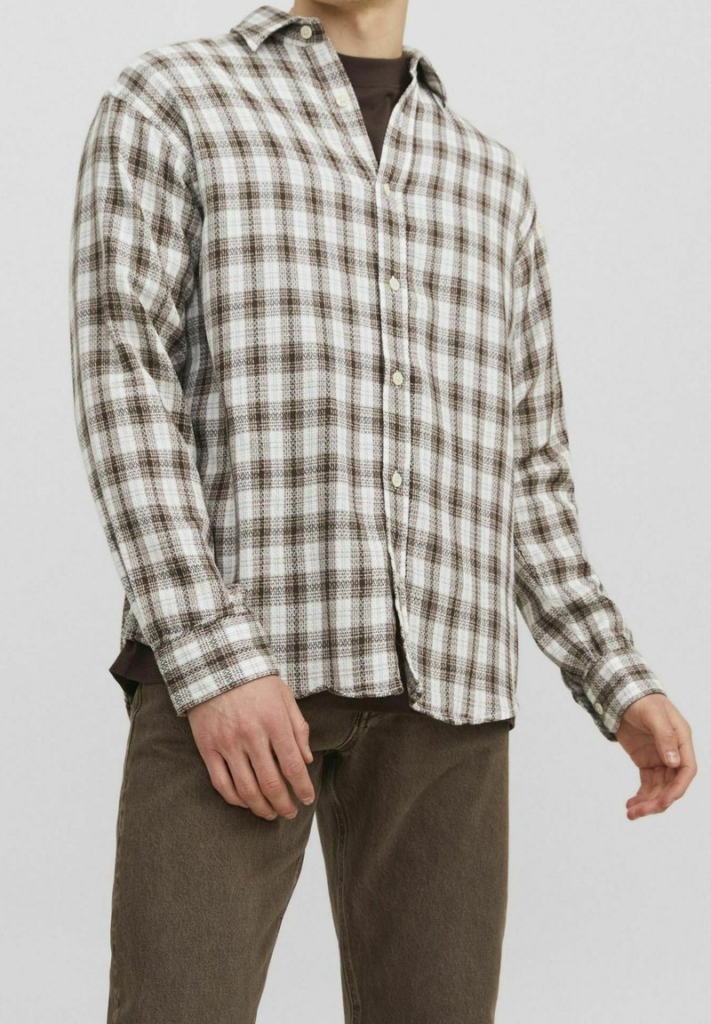 Brun och vit rutigt flanellskjorta med knäppning fram, långa ärmar och avslappnad passform. Bärs över en mörk t-shirt med rund hals.