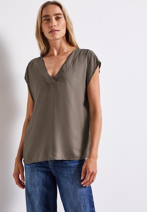 Olive green v-neck blouse with short sleeves, smooth texture, and a relaxed fit, paired with blue denim jeans.