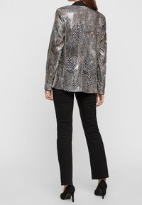 Metalický stříbrný blejzr s hadím vzorem, s černým límcem a upraveným střihem. Nesený přes černé džíny a na vysokých podpatcích.