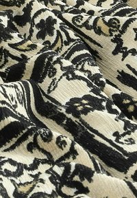 Tissu noir et crème avec des motifs floraux et des volutes complexes, présentant une surface texturée et des rayures alternées.