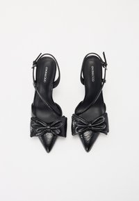 Escarpins en cuir noir à bride arrière avec un bout pointu, présentant un grand nœud sur le devant et une fine sangle autour de la cheville.