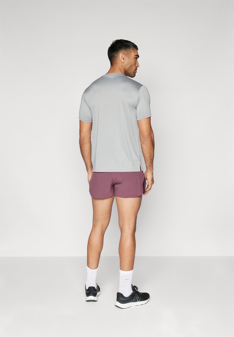 Camiseta atlética de manga corta gris claro, pantalones cortos burdeos, zapatillas deportivas negras, calcetines blancos. Presenta un corte ajustado y aberturas laterales en el dobladillo.