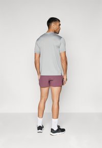T-shirt de sport gris à manches courtes avec fentes sur les côtés, associé à un short bordeaux et des baskets noires. Des chaussettes de sport blanches complètent la tenue.