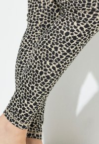 Leggings con motivo a fondo beige e macchie di leopardo nere, realizzate in tessuto elastico, che terminano alla caviglia con un orlo liscio.