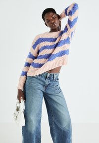 Maglione a maglia con strisce rosa e blu, vestibilità ampia. Abbinato a jeans a vita alta di un leggero blu e a una piccola borsa bianca.