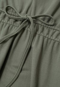 Olive zielony materiał o teksturowanej powierzchni, z wiązanym troczkiem w pasie i marszczonym elastycznym detalem powyżej.