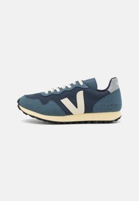 Blue mesh and suede sneaker with cream laces and a large white V logo on the side. Black rubber sole and light grey heel detail.