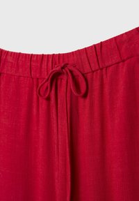Ceinture élastique rouge avec un cordon noué sur un vêtement en tissu texturé.