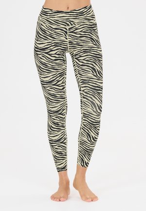 Kvinde iført højtaljede zebra-print leggings, stående barfodet med fødderne tæt sammen på en simpel hvid baggrund.