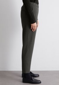 Pantaloni grigi con motivo, dalla linea dritta, realizzati in tessuto testurizzato. Vita aderente, tasche laterali e indossati con mocassini neri e calze.