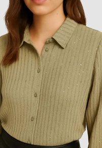 Camicia button-up a coste verde oliva con una finitura strutturata, caratterizzata da sottili accenti scintillanti e un design classico del colletto.