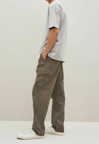 T-shirt grigia a maniche corte abbinata a pantaloni cargo verde oliva con numerose tasche e sneakers bianche a vita bassa. Design semplice e funzionale.