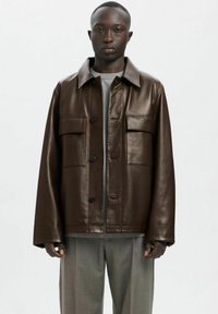 Rjava usnjena jakna z ovratnikom, dvema sprednjima žepoma in zapiranjem na gumbe. Model nosi sivo majico in svetlo sive hlače.