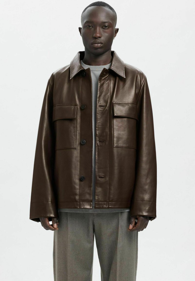 Rjava usnjena jakna z ovratnikom, dvema sprednjima žepoma in zapiranjem na gumbe. Model nosi sivo majico in svetlo sive hlače.