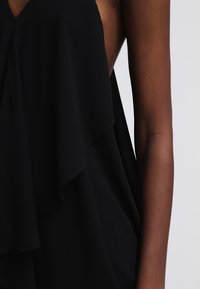 Sort bluse med lagdelt, flydende stof. Blødt, let materiale svøber sig om halsen og armene og skaber en elegant silhuet.