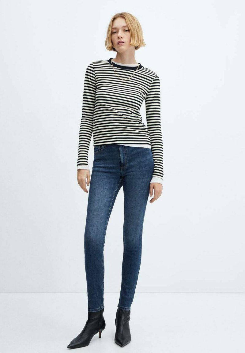 Schwarz-weiße gestreifte Langarmbluse, taillierte Form, kombiniert mit blauen Skinny-Jeans und schwarzen spitzen Ankle-Boots. Einfache goldene Halskette als Akzent.