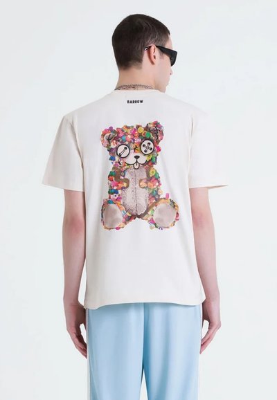 T-shirt bianco a maniche corte con una grafica colorata di un orsetto sul retro, decorato con diverse forme e motivi vivaci.