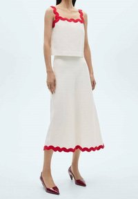 Conjunto de dos piezas blanco con ribete rojo en forma de ola, que presenta un top recortado con tirantes anchos y una falda hasta la rodilla. Tacones rojos brillantes.